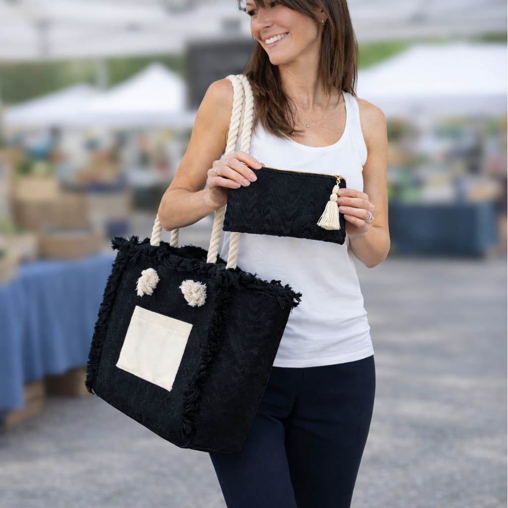 Woman holding a black tote bag with white patches at an outdoor market.